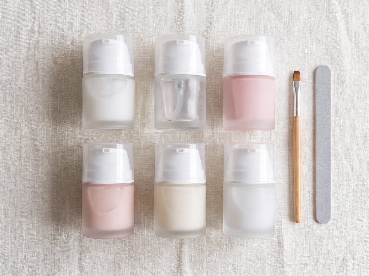 Six unlabeled frosted glass pump jars of builder gel in white, clear, pink and ivory shades with a gel brush and nail file on linen