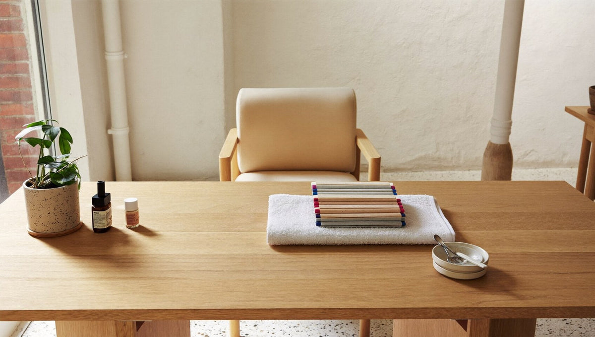 A calm, minimalist nail technician's workstation in a bright studio with a light oak desk, a folded towel and a plant