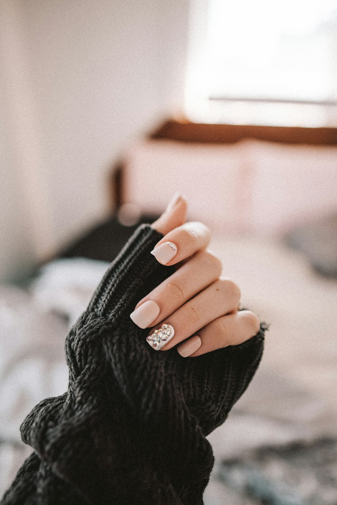 Hand in een zwarte gebreide mouw met nude nagels en één accentnagel met een klein zilveren design.