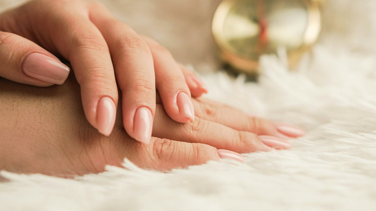 Hand with glossy rosy nude almond nails resting on white faux fur, a gold clock blurred in the background
