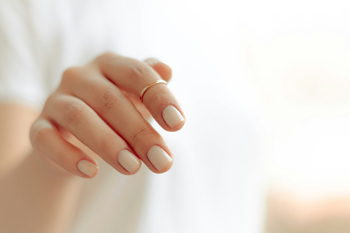 Hånd med en blank, nude gelmanicure på korte, runde negle mod en hvid baggrund