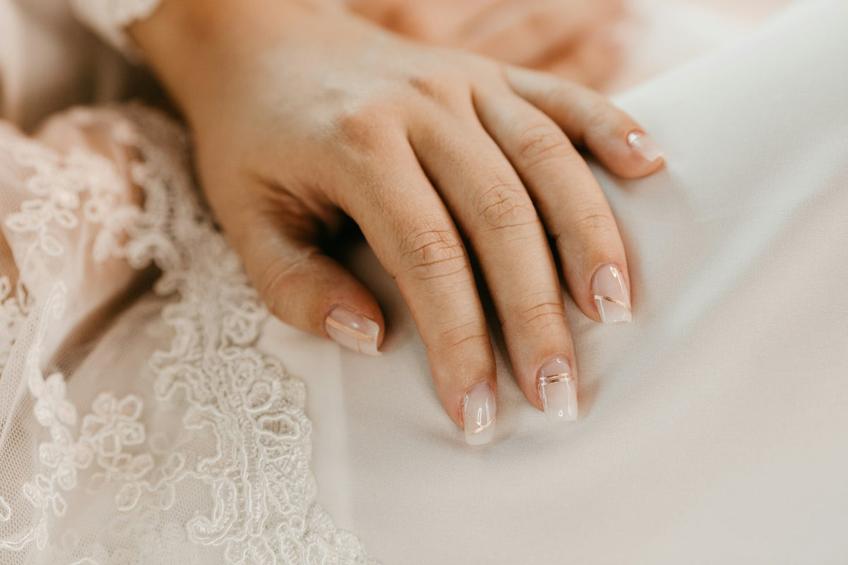 Bride's hands with a soft French manicure resting on a lace and satin dress