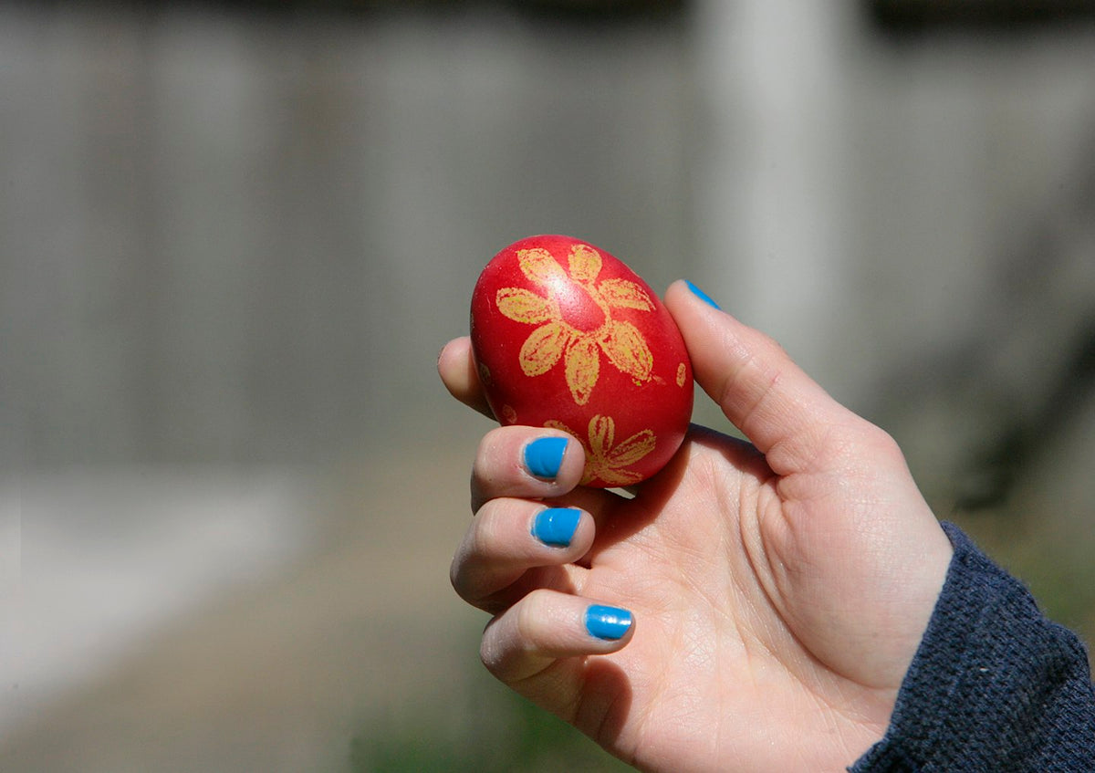 Hand with bright blue nails holding a red hand-painted Easter egg