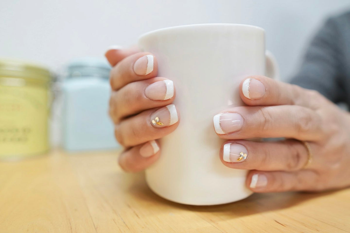 Hands with short nude and white French nails holding a white mug on a wooden table