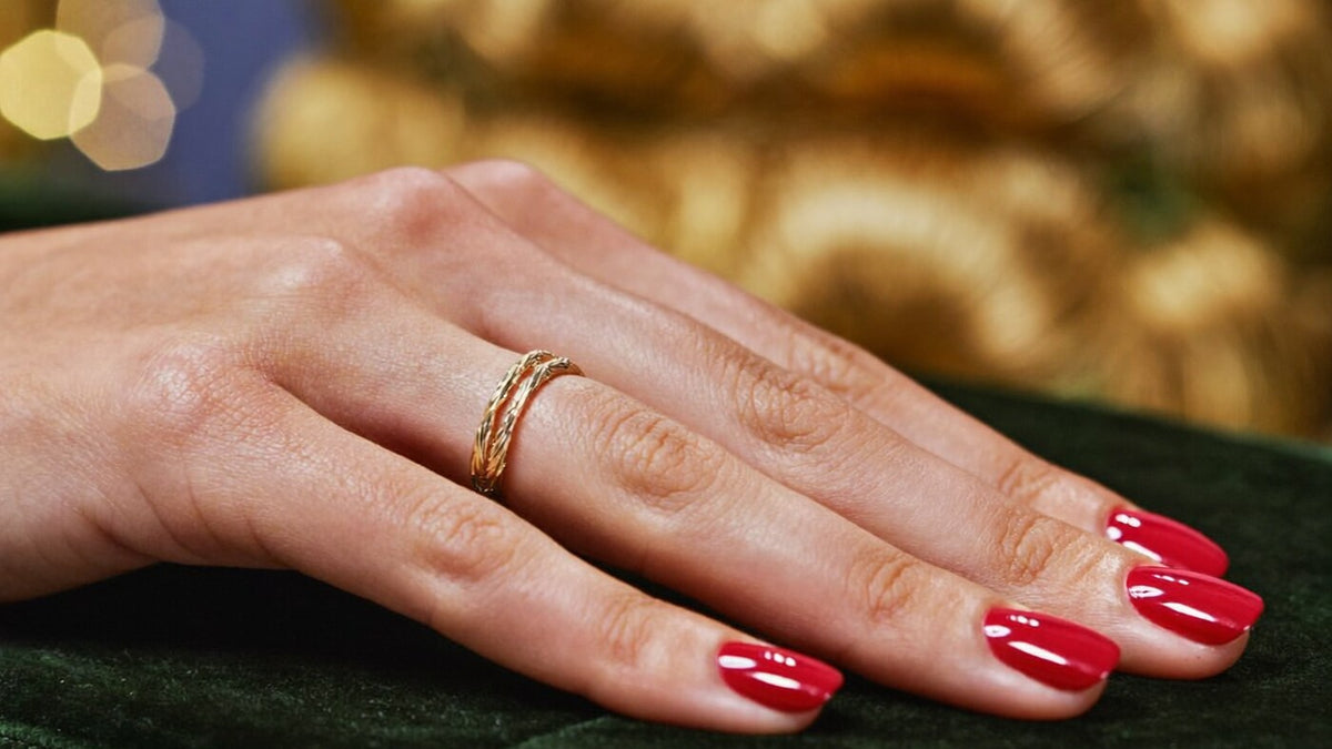 Glossy classic red almond nails with a fine gold ring on deep green velvet, warm golden lights in the background