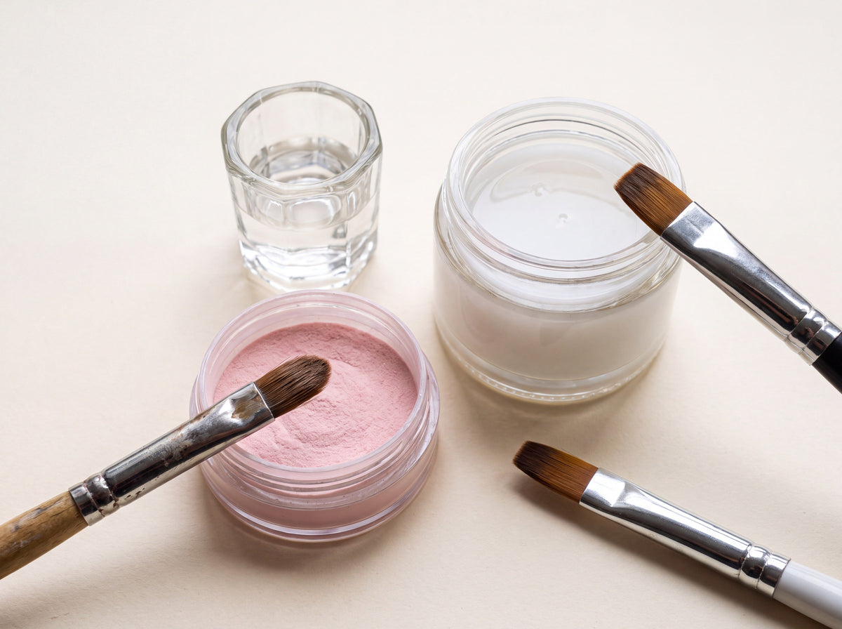 Dappen dish of liquid monomer and pink acrylic powder with brushes next to an unlabeled jar of milky builder gel