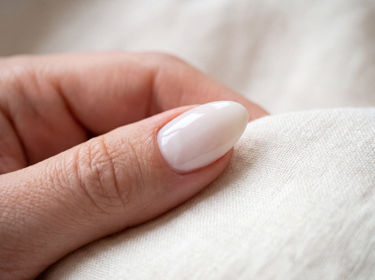 Side view of a natural almond nail with a glossy milky white gel overlay and a soft curved apex