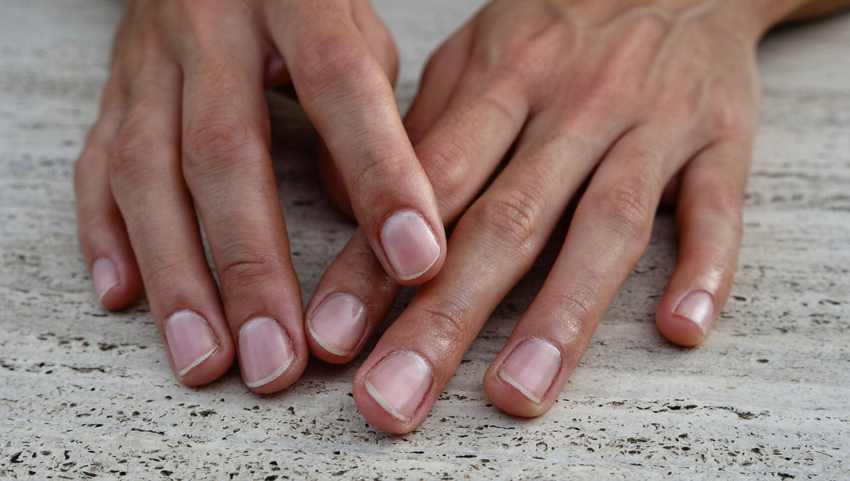 Two relaxed hands with short, bare, healthy natural nails resting on pale travertine stone