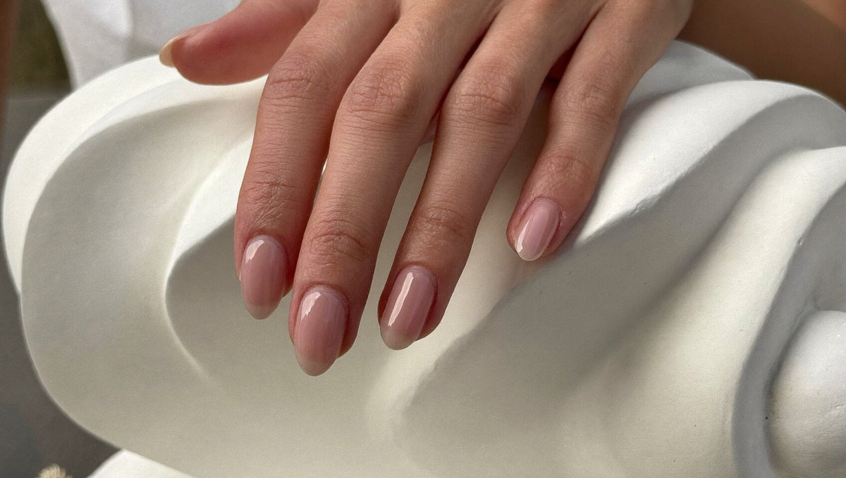 Elegant hand with medium oval nails in a glossy rosy nude resting on a sculptural ivory plaster surface