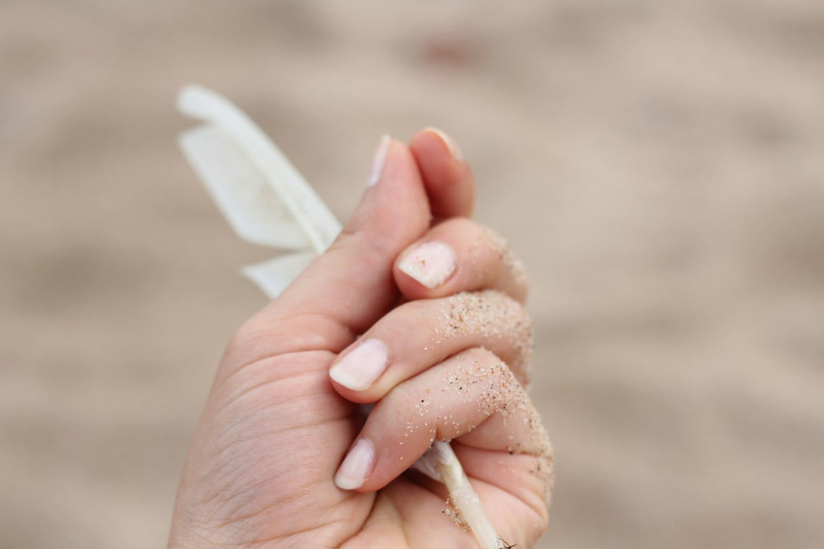 Hand with bare natural nails holding a white nail file against a sandy background
