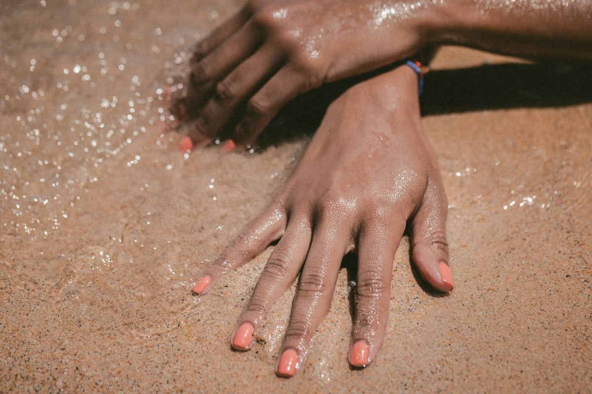 Hands with coral nails resting on wet, sparkling sand