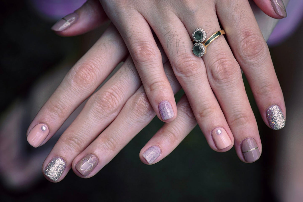 Hands with short pastel gel nails in pink, lilac and glitter, with silver rings