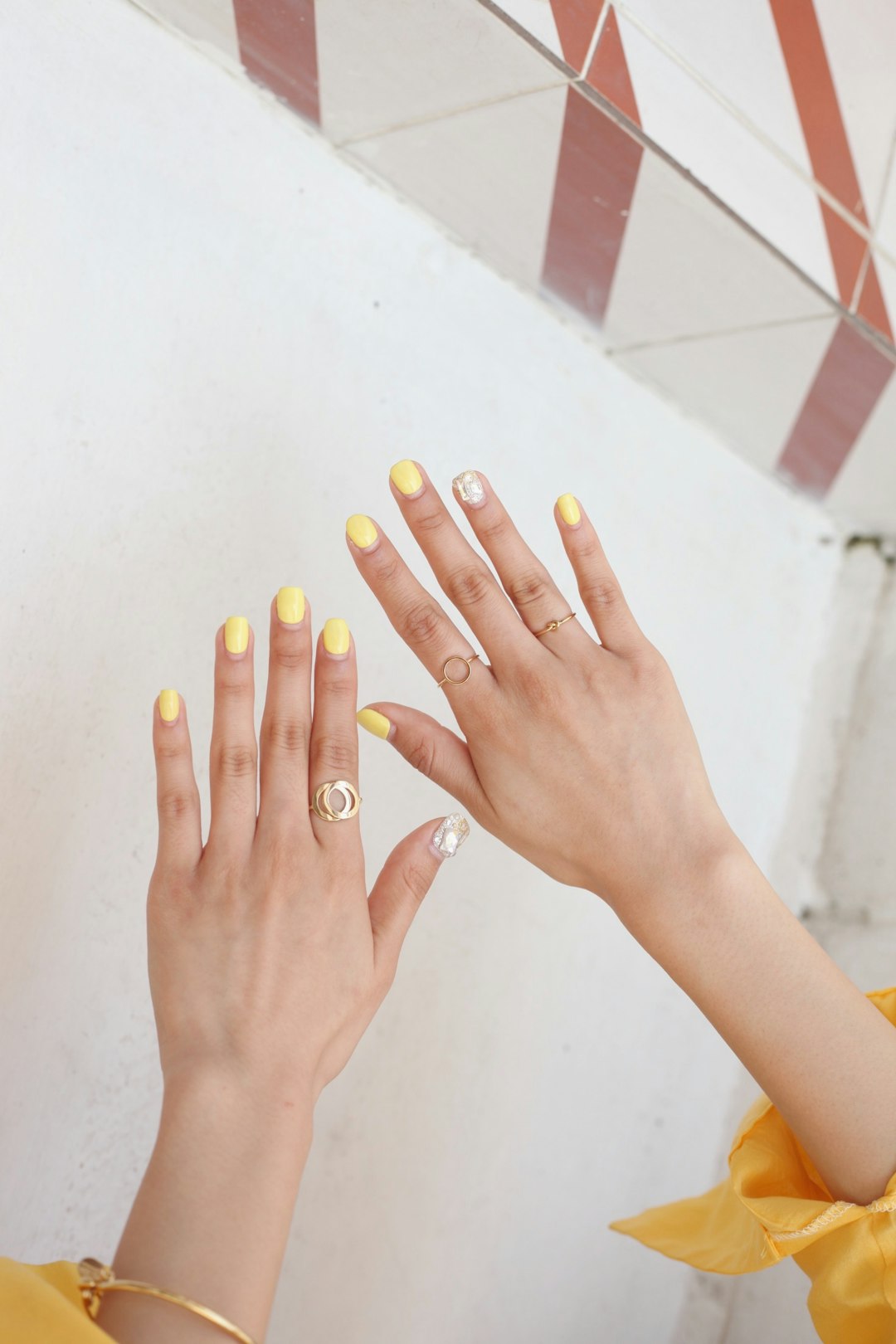 Hands with pale yellow nails raised against a white wall