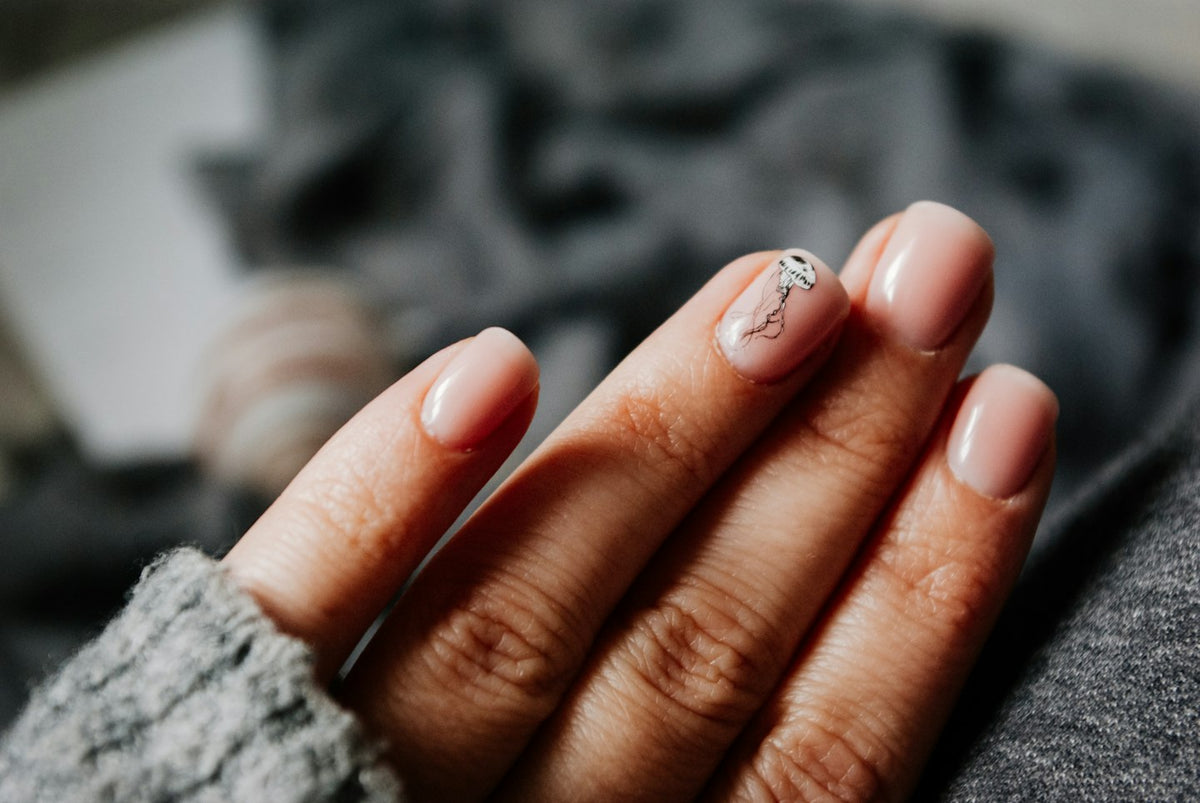 Hand with pale pink nails and a fine silver line accent against a grey knit sleeve
