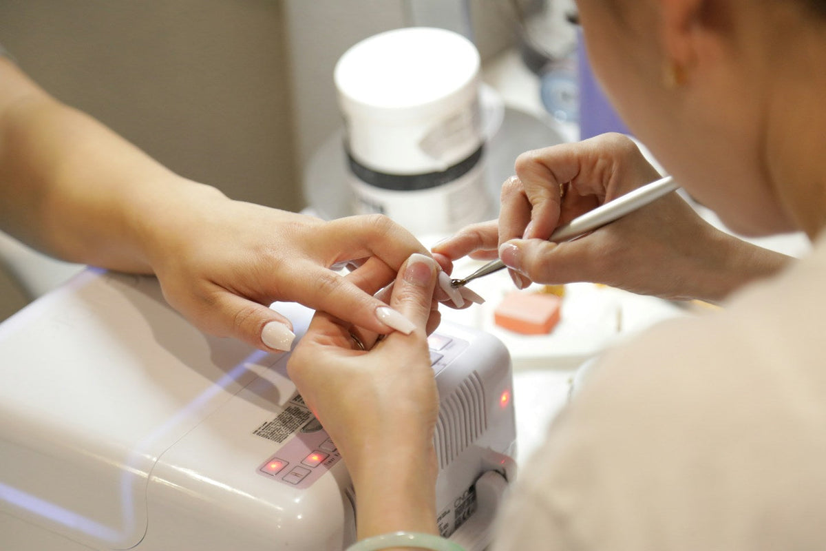 Nail technician pushing back a client's cuticles before a gel manicure, a lamp in the foreground