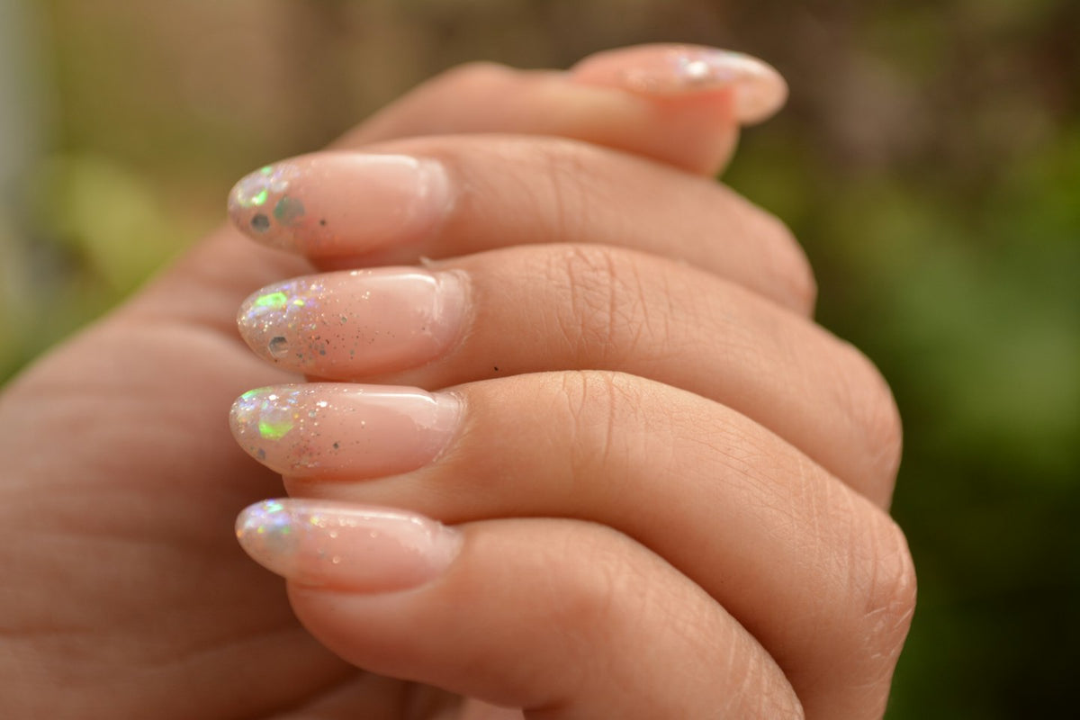 Hands with sheer nude gel nails and glitter tips against a green background