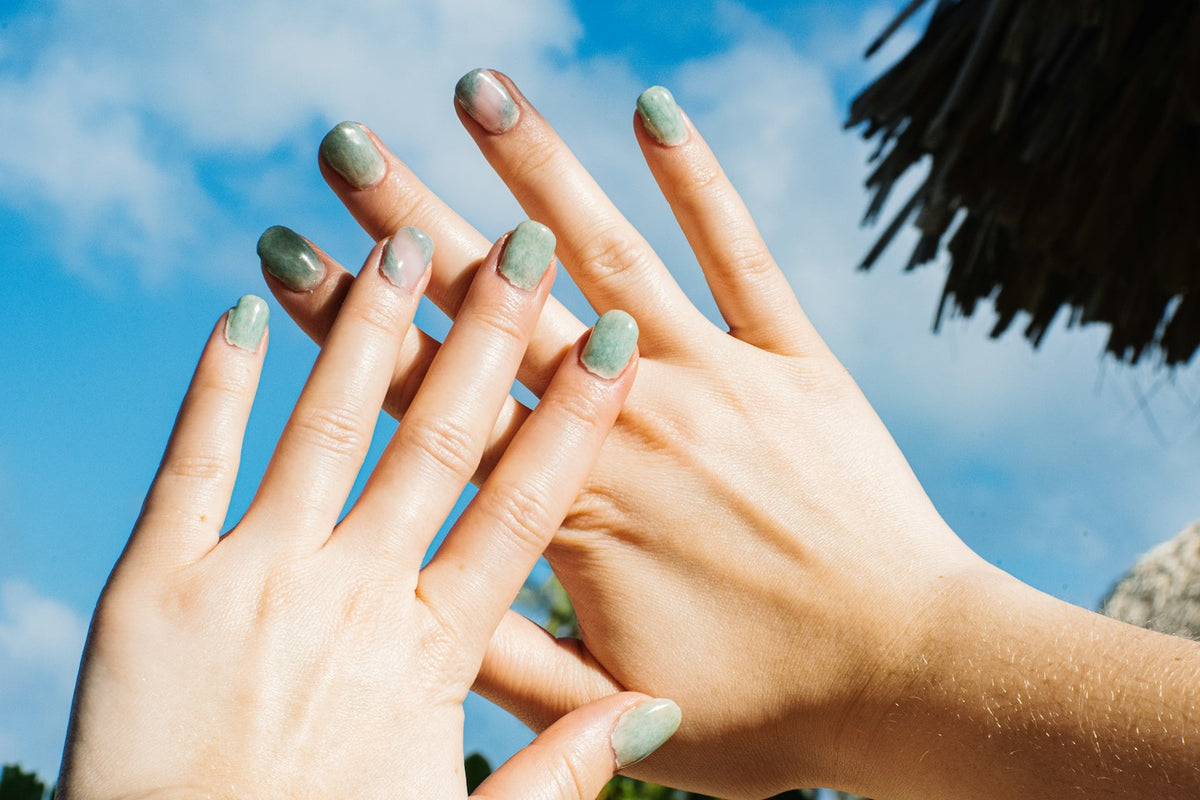 Two hands with glossy jade green nails against a bright blue sky