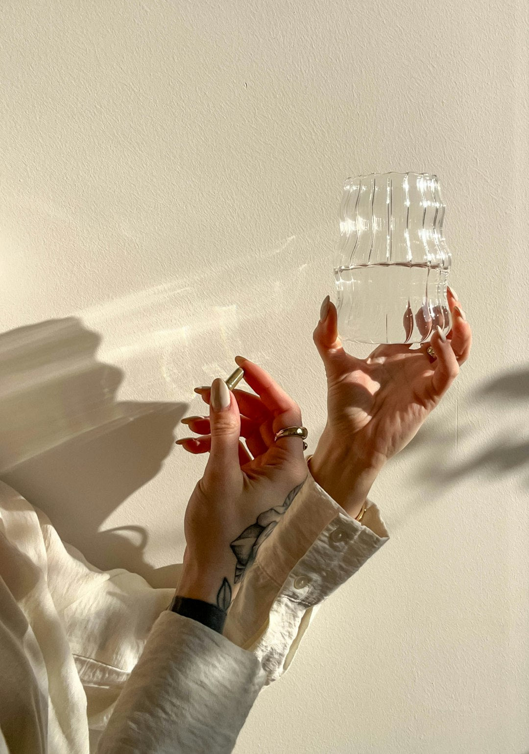 Hands with glossy red nails holding a clear ribbed glass in soft sunlight