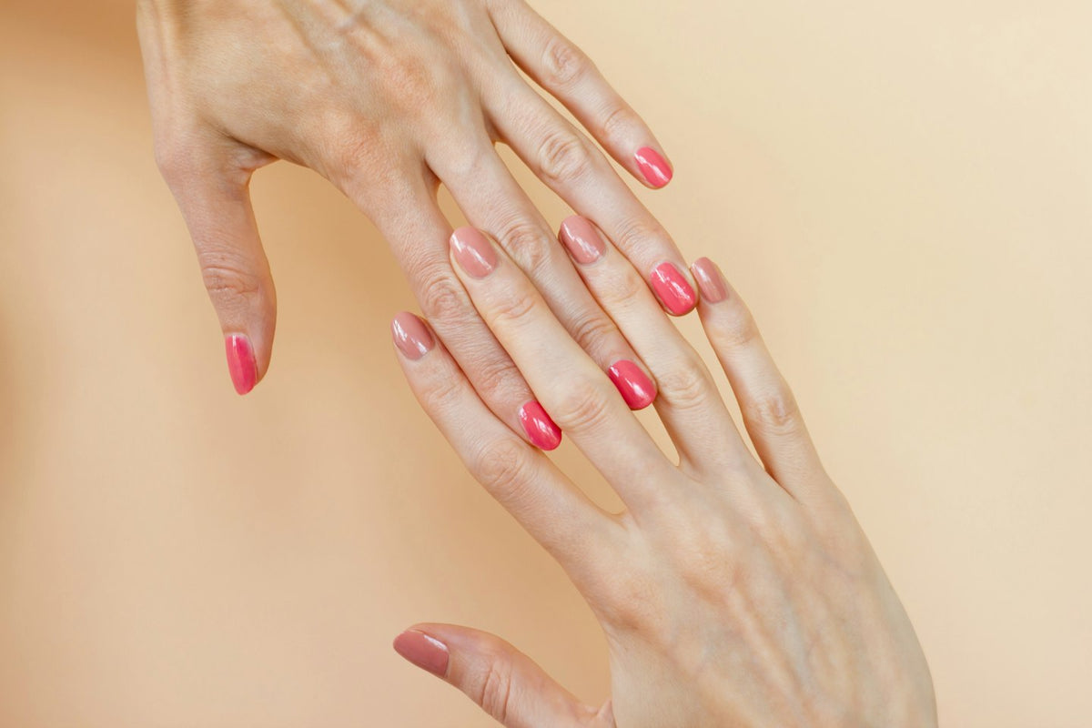 Two hands with coral pink nails against a peach background