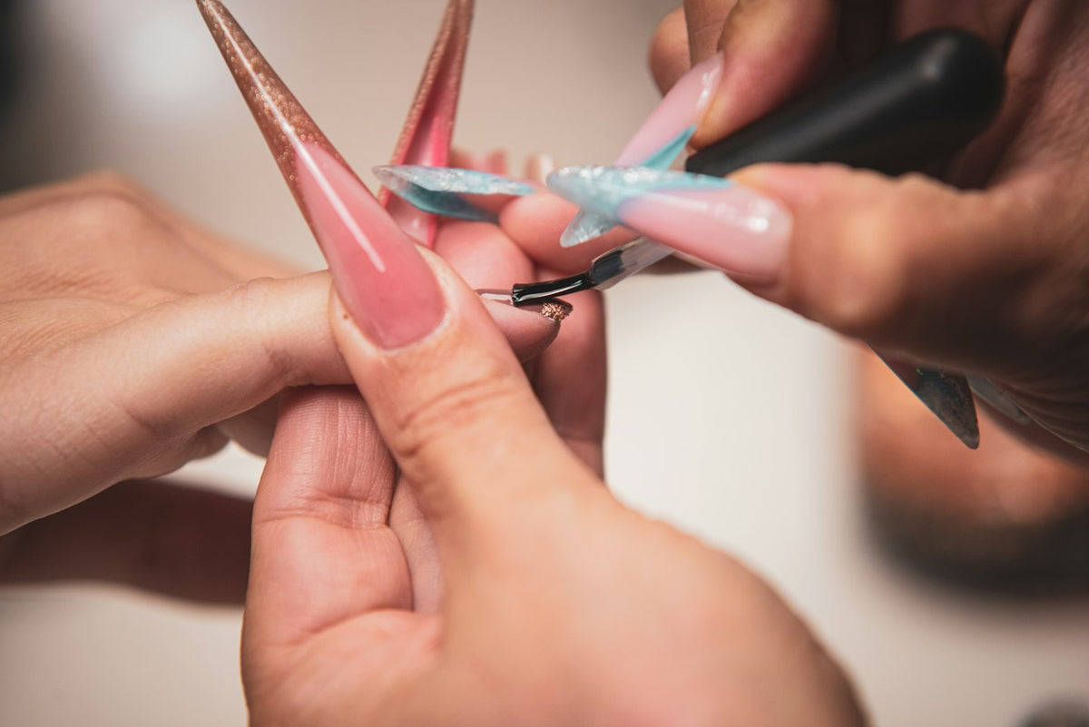 Nail technician shaping long pink stiletto extensions with a file