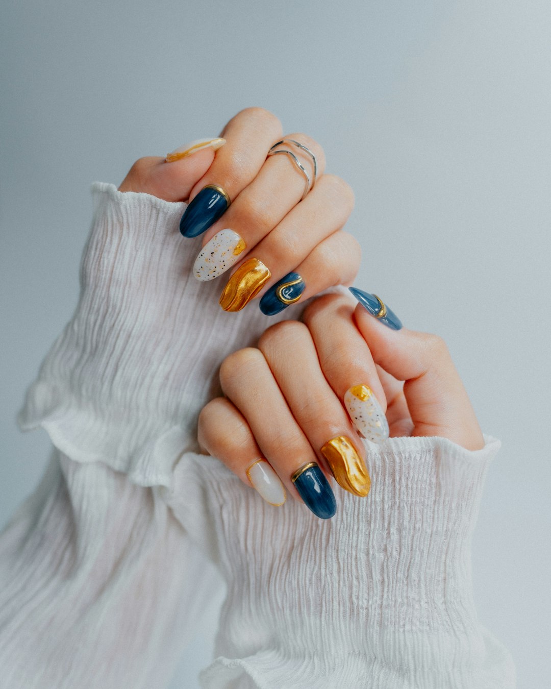 Hände in weißer Rüschenbluse mit marineblauer, goldener und weißer Nailart auf mandelförmigen Nägeln