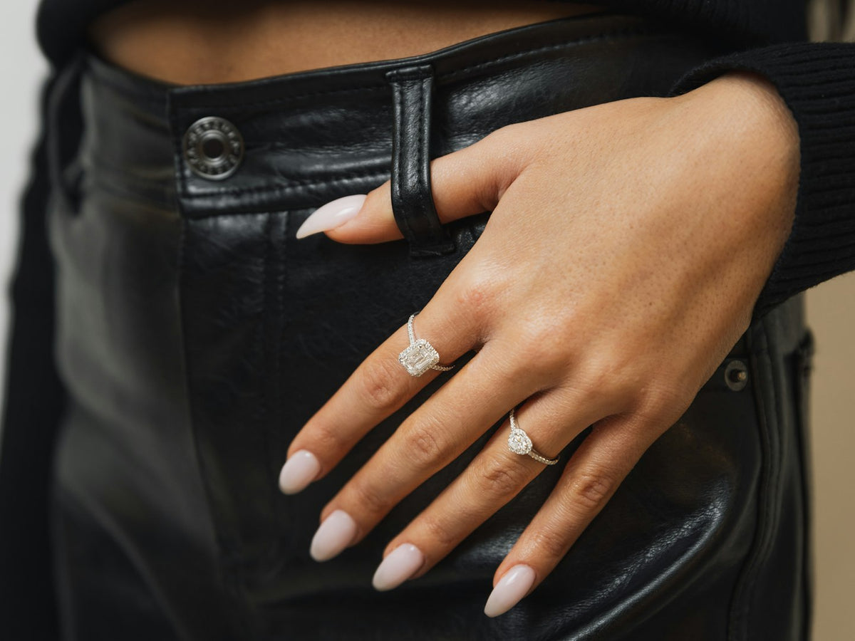 Hand with milky white almond nails and fine silver rings against black leather