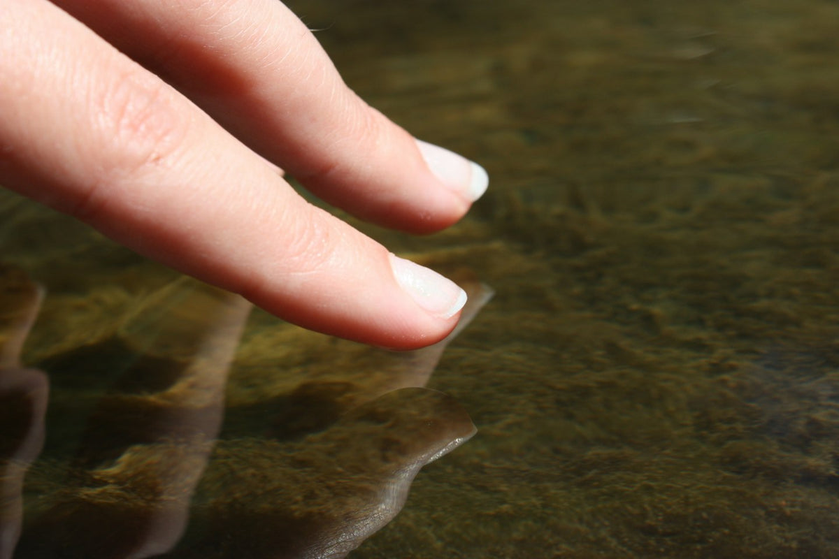 Doigts aux ongles naturels, clairs et brillants, qui effleurent la surface de l'eau