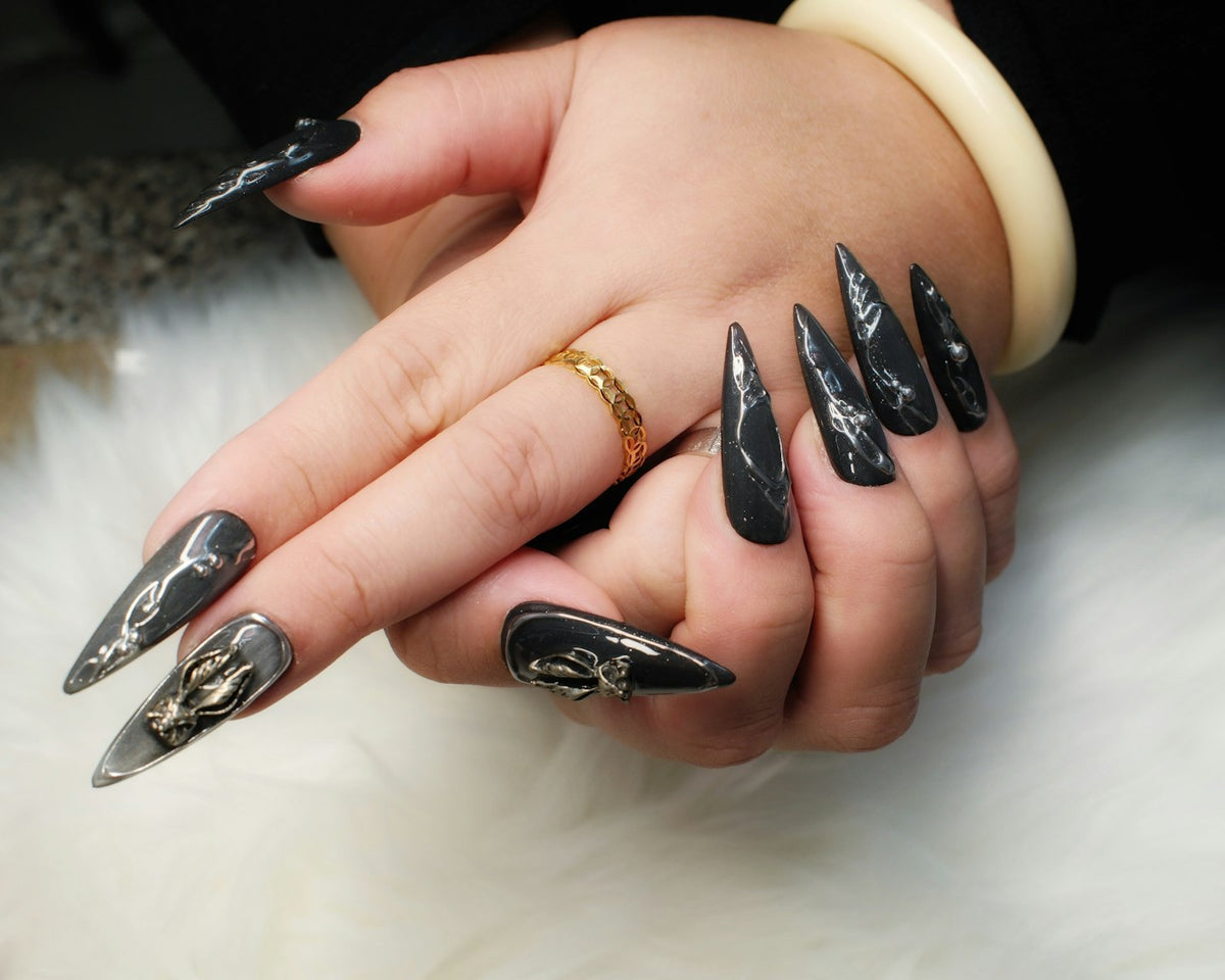 Hands with long black and grey marble stiletto nails with gold details on white fur
