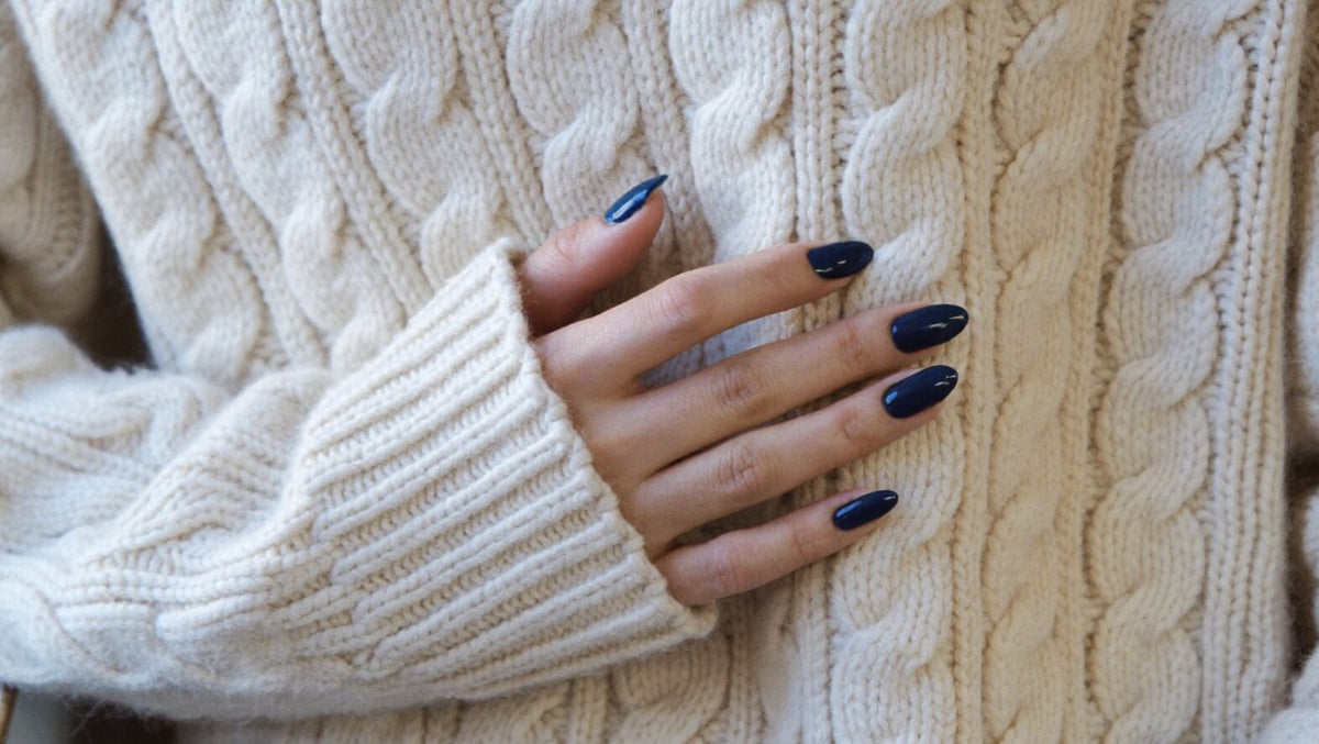 Hand with short almond nails in a glossy deep navy resting on a cream cable-knit sweater