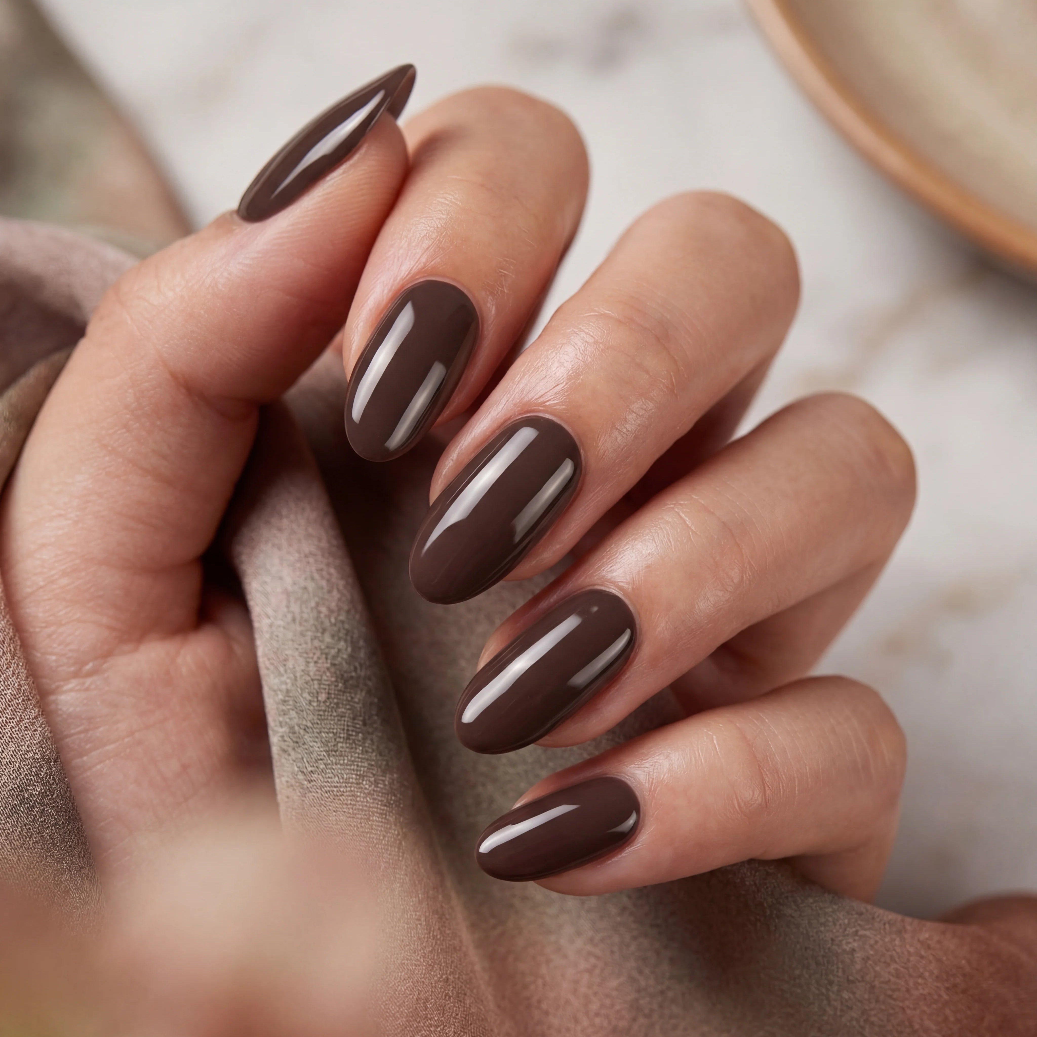 Close-up of a hand with brown nail polish on a neutral background