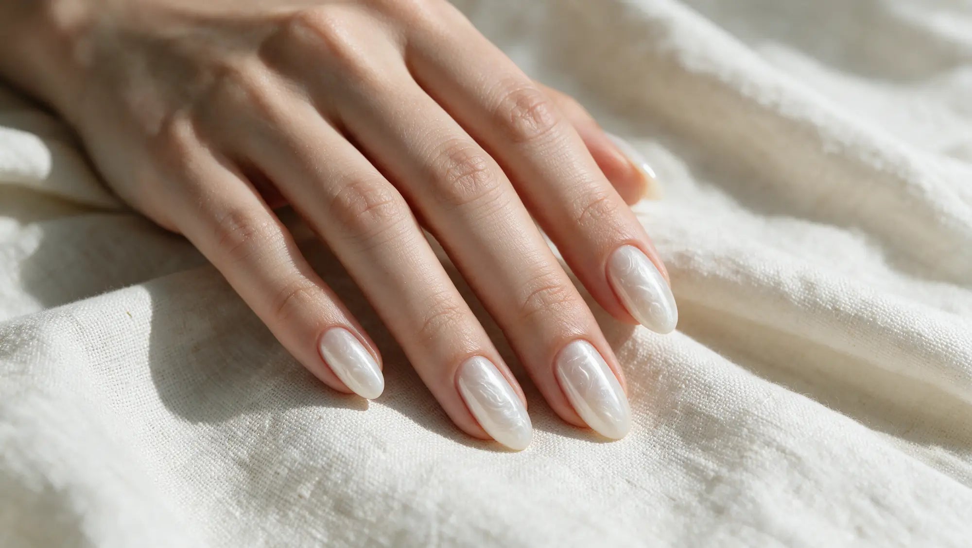 A finished milky pearl manicure resting on ivory linen