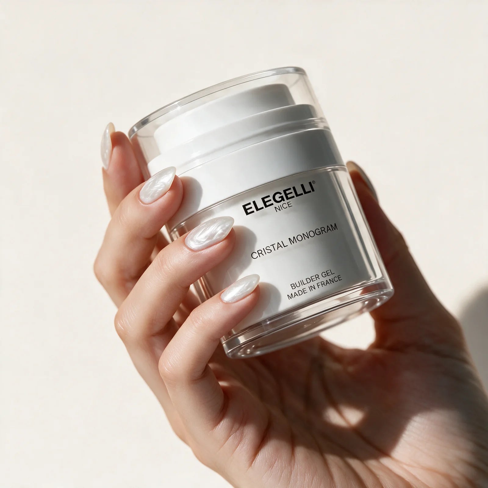 A manicured hand holding the jar against ivory